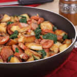 Closeup of a skillet of fried sausage and potatoes with spinach